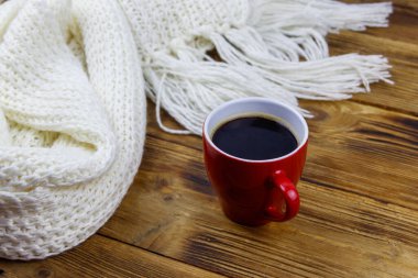 Ahşap masada örülmüş beyaz eşarp ve bir fincan kahve. Kış konsepti