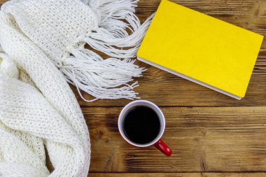 Ahşap masada örülmüş beyaz eşarp, kitap ve bir fincan kahve. Üst Manzara. Kış konsepti