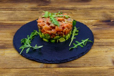 Avokado ve roka ile ahşap masada somon tartar.