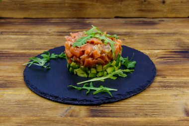 Avokado ve roka ile ahşap masada somon tartar.