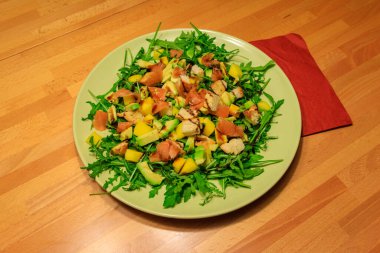 Tahta bir masada mango, avokado, somon, roka ve kızarmış ekmekle taze sağlıklı salata.