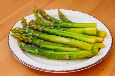 Ahşap bir masada yeşil haşlanmış kuşkonmaz.
