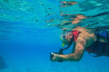 Fotoğraf makineli bir adam fotoğraf çekiyor ve Mısır 'da, Kızıl Deniz' de mercan resifi altında şnorkelle yüzüyor.