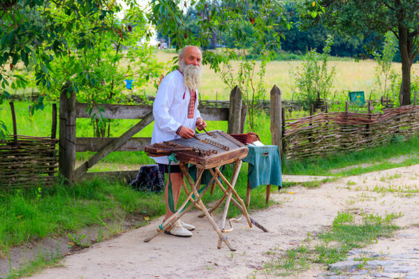 Kiev, Ukraine - June 28, 2020: Old ukrainian man playing gusli in Pyrohiv (Pirogovo) village near Kiev, Ukraine