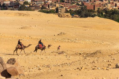 Kahire, Mısır - 8 Aralık 2018: Kahire şehir manzarasına karşı Giza platosunda deveye binen turistler