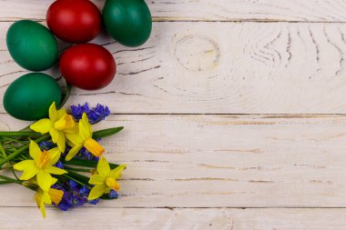 Boyanmış Paskalya yumurtaları, sarı nergis buketi ve beyaz ahşap arka planda mavi scilla çiçekleri. Paskalya kompozisyonu. Üst görünüm, alanı kopyala