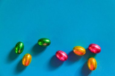 Mavi arka planda folyo içinde paskalya çikolatası yumurtaları. Üst görünüm