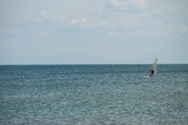 Rüzgar sörfü. Sakin denizde ya da okyanusta egzersiz yapan bir sörfçü. Yaz tatili boyunca eğlence amaçlı su sporları