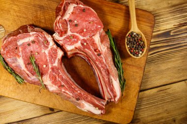 Kemiğin üzerinde çiğ biftek, baharatlar ve ahşap masada biberiye. Üst görünüm