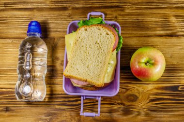 Sandviçli beslenme çantası, ahşap bir masada bir şişe su ve elma. Üst görünüm