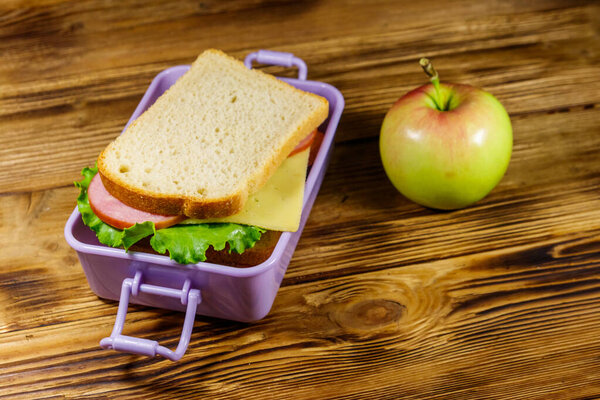 Коробка с бутербродами и яблоком на деревянном столе