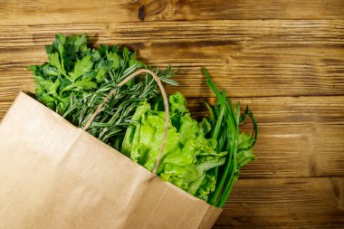 Yeşil soğanlı kağıt torbası, biberiye, marul yaprakları ve ahşap masada maydanoz. Üst Manzara. Sağlıklı gıda ve market alışverişi kavramı