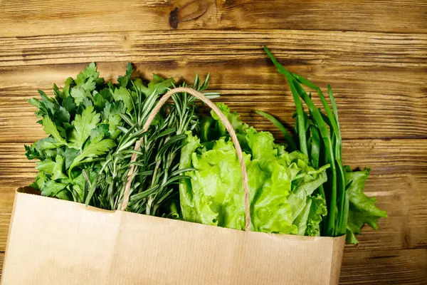 Yeşil soğanlı kağıt torbası, biberiye, marul yaprakları ve ahşap masada maydanoz. Üst Manzara. Sağlıklı gıda ve market alışverişi kavramı