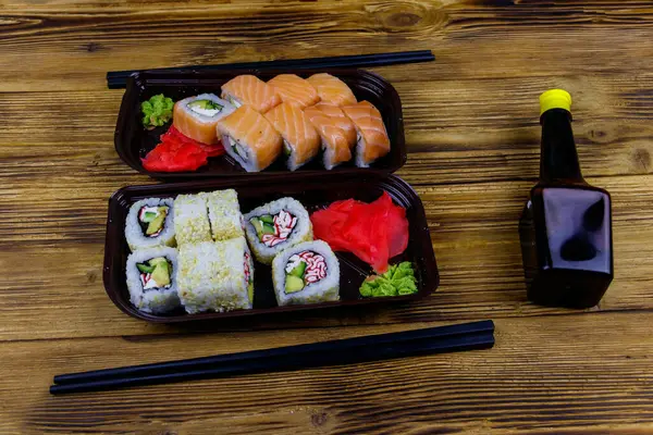 Set of sushi rolls in plastic boxes, soy sauce and chopsticks on wooden table. Sushi for take away or delivery of sushi in plastic containers