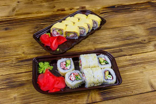Set of sushi rolls in plastic boxes on wooden table. Sushi for take away or delivery of sushi in plastic containers