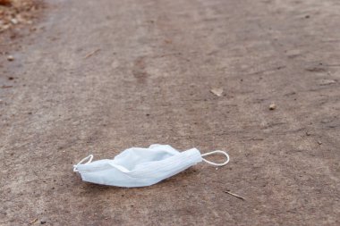 Kirli, tek kullanımlık tıbbi maske. Asfalt sokağa çöp olarak atılmış. COVID-19 sırasında israf. Koronavirüs salgınından kaynaklanan kirlilik