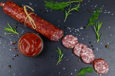 Ketçaplı salam sosisi ve siyah tahtada baharatlar. Üst görünüm