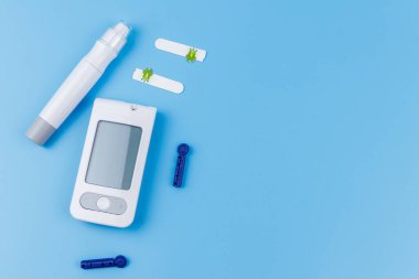 Dijital glukometre, tükenmez kalem, tek kullanımlık iğneler ve pastel mavi arka planda test şeritleri. Üst görünüm, boşluğu kopyala. Diyabet kavramı