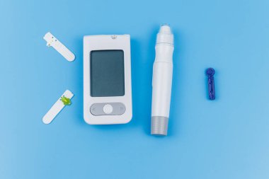 Dijital glukometre, tükenmez kalem, tek kullanımlık iğneler ve pastel mavi arka planda test şeritleri. Üst Manzara. Diyabet kavramı