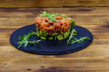Avokado ve roka ile ahşap masada somon tartar.