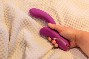 Yatakta pembe vibratör tutan bir kadın eli.