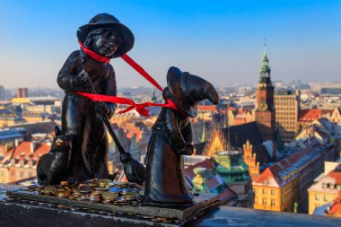 Wroclaw, Polonya - 9 Ocak 2024: Büyücüler Tekla ve Martynka cüceleri St. Mary Magdalene Kilisesi 'nin Tövbe Köprüsü' nde muhteşem Wroclaw şehir manzarasına karşı bozuk paralarla heykeller. En ünlü Wroclaw cücelerinden biri.