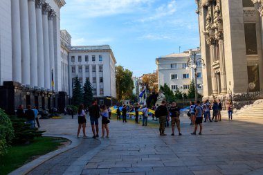 Kiev, Ukraine - August 23, 2019: People holding a huge ukrainian flag near Presidential administration during Day of Flag of Ukraine celebration in Kiev, Ukraine clipart