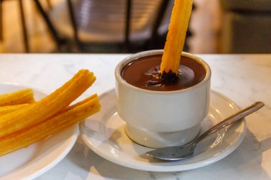 Churros 'u sıcak çikolata bardağına batırmak. Churros - geleneksel İspanyol tatlısı