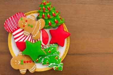 Plate with tasty festive Christmas cookies in the shape of Christmas tree, Gingerbread man, star and Christmas sock on wooden table. Top view clipart