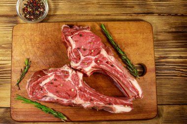 Kemiğin üzerinde çiğ biftek, baharatlar ve ahşap masada biberiye. Üst görünüm