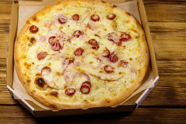 Tahta bir masanın üzerindeki karton kutuda nefis taze pizza. Yemek teslimatı, fast food, pizza teslimatı.