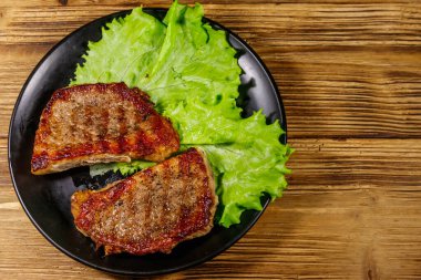 Ahşap masada marul yapraklı ızgara domuz bifteği. Üst görünüm