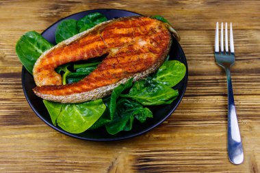 Ahşap masada ıspanaklı ızgara somon bifteği.