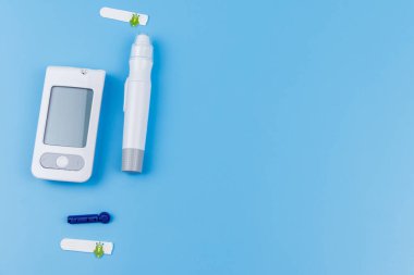Dijital glukometre, tükenmez kalem, tek kullanımlık iğneler ve pastel mavi arka planda test şeritleri. Üst görünüm, boşluğu kopyala. Diyabet kavramı