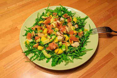 Tahta bir masada mango, avokado, somon, roka ve kızarmış ekmekle taze sağlıklı salata.