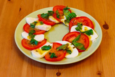 Domatesli İtalyan caprese salatası, ahşap bir masada mozzarella peyniri ve fesleğen.