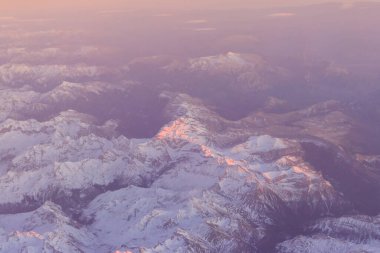 Gün batımında karla kaplı bir dağ sırasının uçak penceresinden bak.