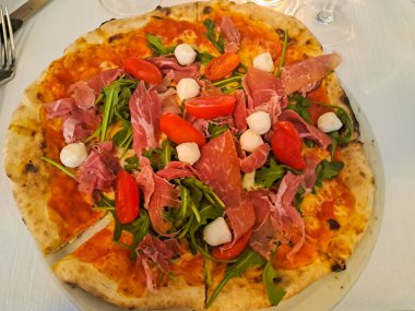 Prosciutto, mozzarella, vişneli domates ve roka ile nefis yuvarlak pizza. Üst görünüm