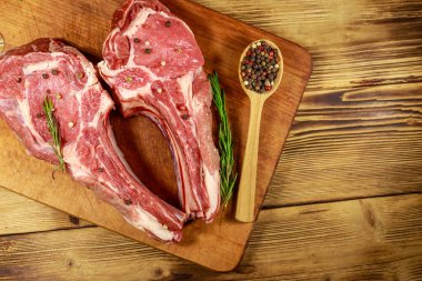 Kemiğin üzerinde çiğ biftek, baharatlar ve ahşap masada biberiye. Üst görünüm