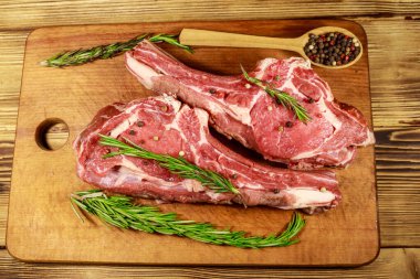 Kemiğin üzerinde çiğ biftek, baharatlar ve ahşap masada biberiye. Üst görünüm