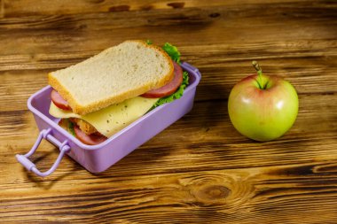 Tahta bir masada, sandviç ve elmayla beslenme çantası.