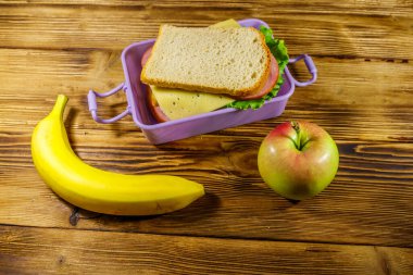 Sandviç, muz ve elmayla birlikte ahşap bir masada.