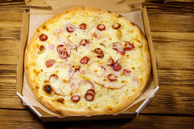 Tahta bir masanın üzerindeki karton kutuda nefis taze pizza. Üst Manzara. Yemek teslimatı, fast food, pizza teslimatı.