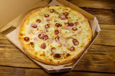 Tahta bir masanın üzerindeki karton kutuda nefis taze pizza. Yemek teslimatı, fast food, pizza teslimatı.