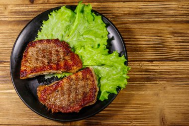 Ahşap masada marul yapraklı ızgara domuz bifteği. Üst görünüm