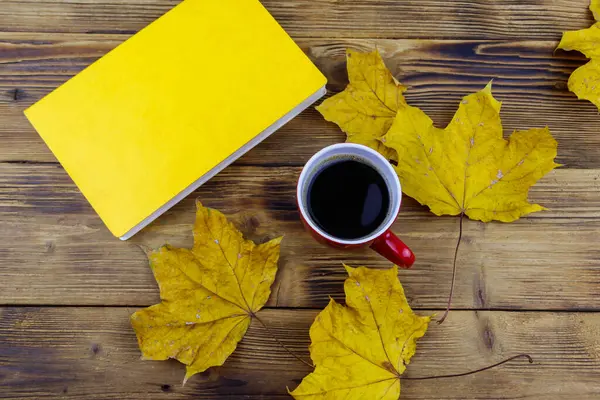 Bir fincan kahve, kitap ve sonbahar akçaağaç yaprakları ahşap masada. Üst Manzara. Sonbahar rahat konsepti
