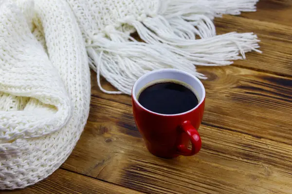 Ahşap masada örülmüş beyaz eşarp ve bir fincan kahve. Kış konsepti