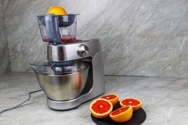 Mutfak masasında modern elektrik sıkacağı ve greyfurt. Taze sıkılmış greyfurt suyu hazırlanıyor.