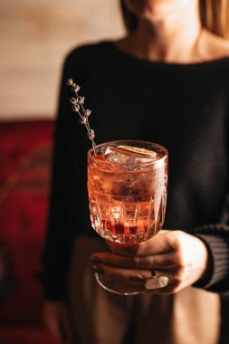 Elinde bir bardak viski ve ahşap masada kokteyl olan bir kadın.