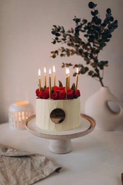 Beyaz bir tabakta mumlu pasta ve güller.